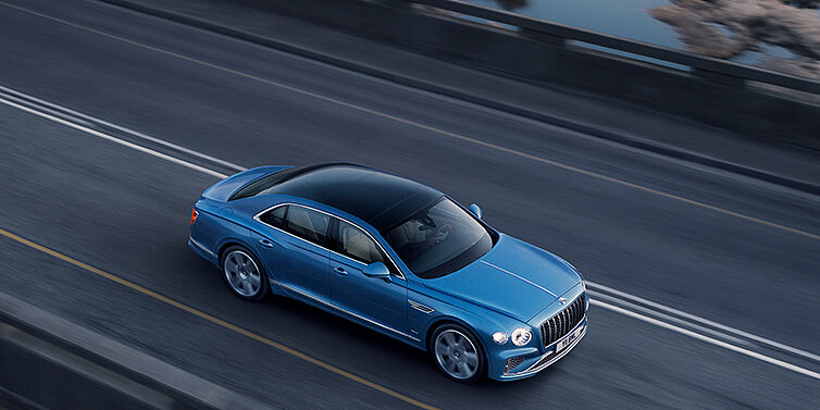 Bentley Kaohsiung New Bentley Flying Spur Azure sedan in Light windsor blue paint by Mulliner, with 22 inch Azure wheels seen from overhead driving dynamically on a country road