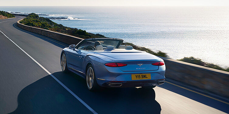Bentley Kaohsiung New Bentley Continental GTC Azure convertible rear view in Light Windsor blue paint with 22 inch ten spoke wheels driving dynamically on an ocean road in the sunshine