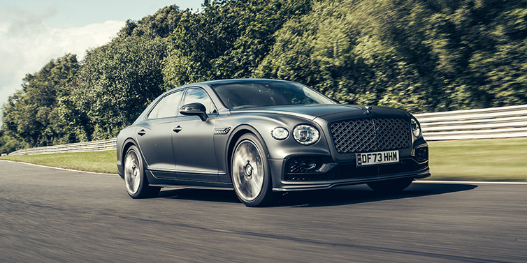 Bentley Kaohsiung Bentley Flying Spur Mulliner sedan front three quarter in dark grey paint driving dynamically by some trees on a track