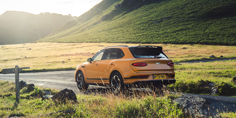 Bentley Kaohsiung Bentley Bentayga S SUV rear three quarter in Sunburst Gold paint on a road surrounded by green hills