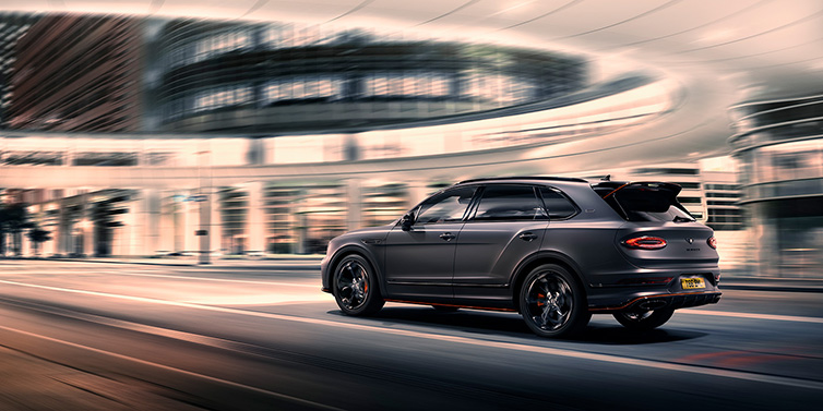 Bentley Kaohsiung Bentley Bentayga S Black Edition SUV rear three quarter in Anthracite Satin paint driving dynamically through a city at night