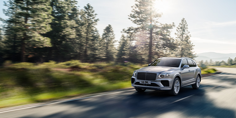 Bentley Kaohsiung Bentley Bentayga SUV front three quarter in Moonbeam silver paint driving dynamically along a tree-lined road