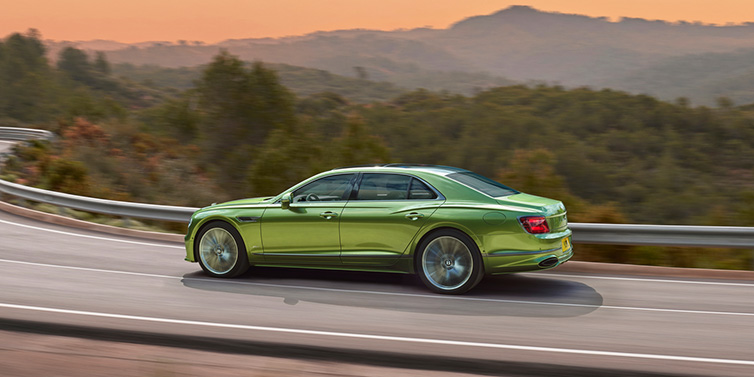 Bentley Kaohsiung Bentley Flying Spur Speed sedan side profile in Tourmaline Green paint driving dynamically on a mountain road at sunset