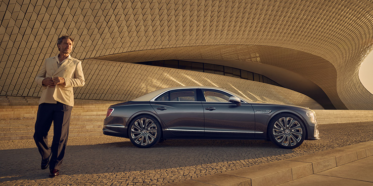 Bentley Kaohsiung Bentley Flying Spur Mulliner sedan in Rose Gold over Magnetic duotone paint parked by a curved wall with person in suit jacket standing on the left